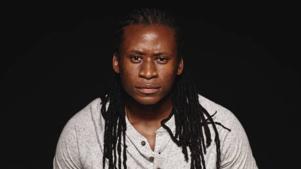 African male with dreadlocks isolated on black background. Portrait of man looking at camera.